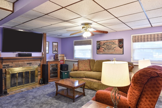 living room with a drop ceiling, a brick fireplace, carpet floors, and ceiling fan