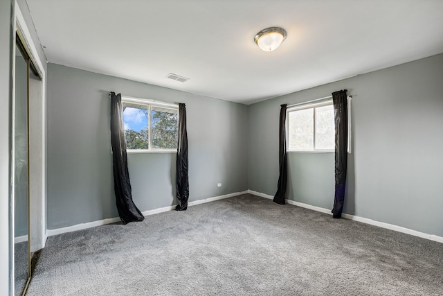 empty room featuring a healthy amount of sunlight, carpet flooring, baseboards, and visible vents
