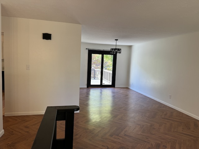 spare room featuring a notable chandelier and dark parquet floors