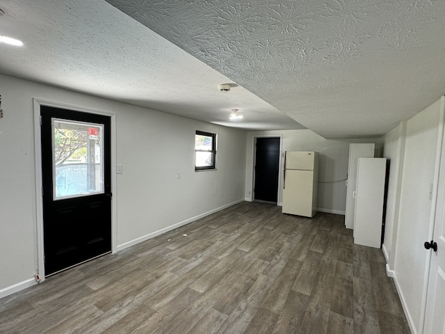 basement featuring a textured ceiling, white fridge, wood-type flooring, and plenty of natural light