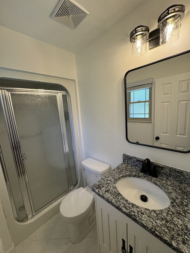 bathroom with a shower with door, a textured ceiling, toilet, vanity, and tile patterned flooring