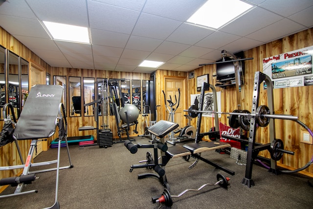 exercise room featuring wooden walls, a drop ceiling, and carpet flooring