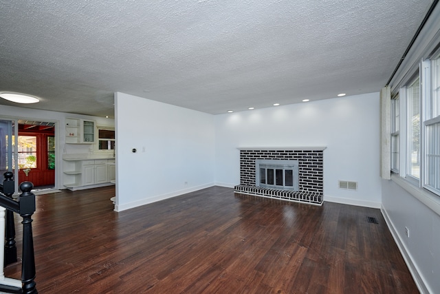 unfurnished living room with a textured ceiling, dark wood-type flooring, and a brick fireplace