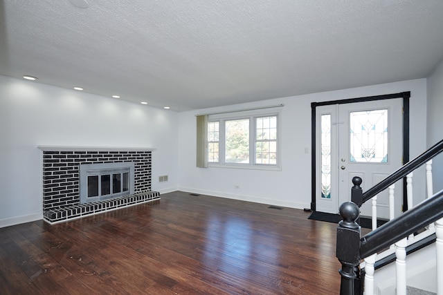 unfurnished living room with a textured ceiling, dark hardwood / wood-style flooring, and a brick fireplace