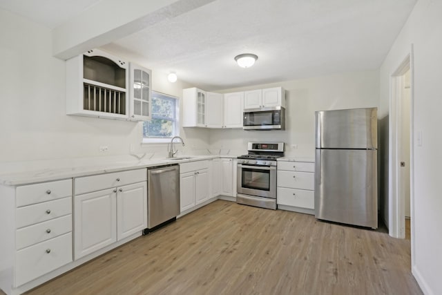 kitchen with light stone countertops, sink, stainless steel appliances, white cabinets, and light hardwood / wood-style flooring