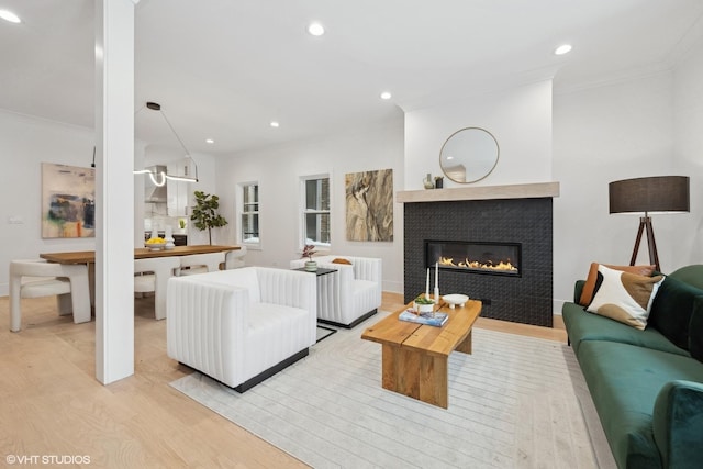 living room featuring light wood-type flooring, crown molding, and a tile fireplace