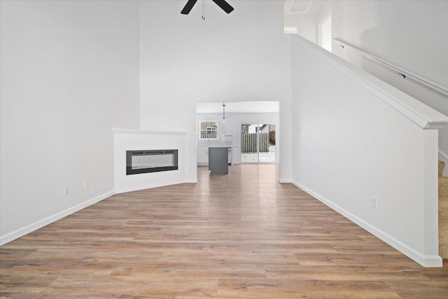 unfurnished living room featuring ceiling fan, a towering ceiling, and light wood-type flooring