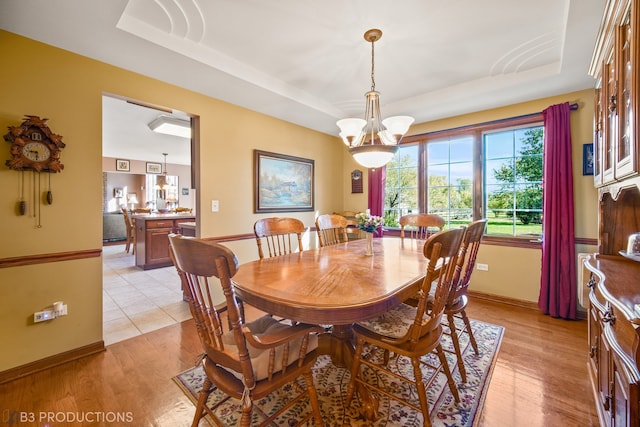 dining room with light hardwood / wood-style floors, a notable chandelier, and a tray ceiling