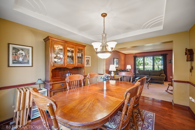 dining room featuring dark wood-type flooring, a tray ceiling, and a chandelier