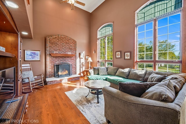 living room featuring a healthy amount of sunlight, a towering ceiling, wood-type flooring, and a brick fireplace