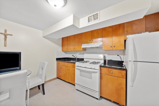 kitchen with a sink, dark countertops, visible vents, under cabinet range hood, and white appliances