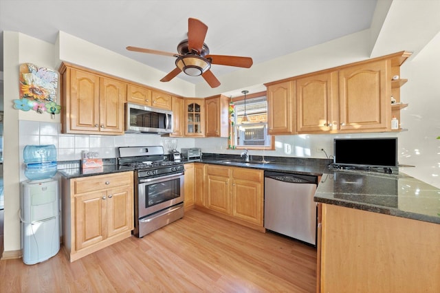 kitchen with dark stone counters, a sink, light wood-style floors, stainless steel appliances, and a ceiling fan