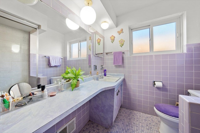 bathroom featuring tile patterned flooring, tile walls, a wainscoted wall, toilet, and vanity