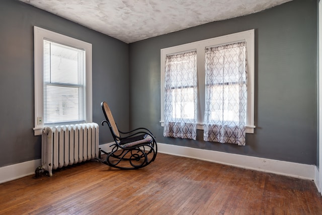 living area with radiator heating unit, hardwood / wood-style flooring, and a textured ceiling