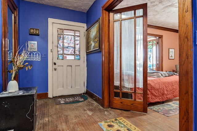 doorway with crown molding, a textured ceiling, and wood-type flooring