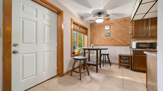 kitchen featuring backsplash, a textured ceiling, ceiling fan, wooden walls, and light tile patterned floors