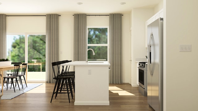 kitchen with a center island with sink, appliances with stainless steel finishes, white cabinetry, a breakfast bar area, and dark hardwood / wood-style floors