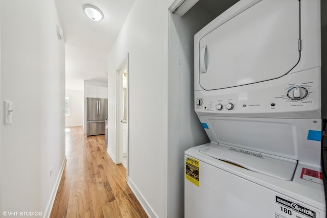 laundry room with light wood finished floors, stacked washer and dryer, baseboards, and laundry area