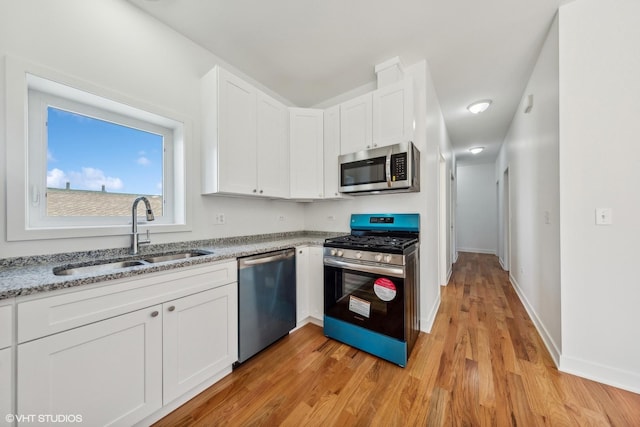 kitchen featuring light stone counters, a sink, light wood-style floors, stainless steel appliances, and white cabinetry