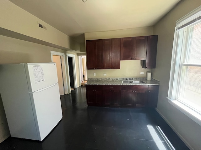 kitchen with dark brown cabinetry, white fridge, and sink