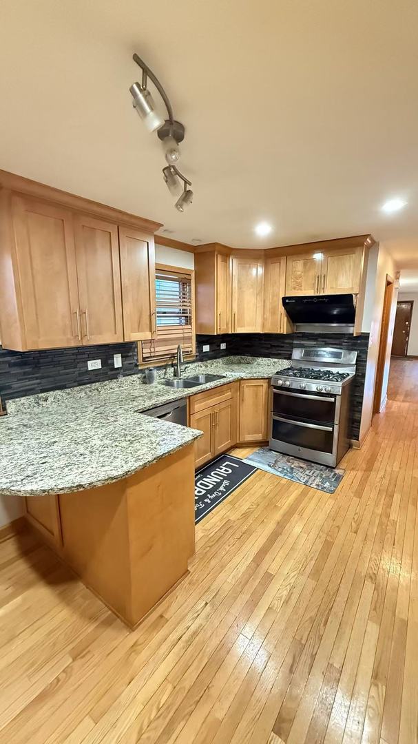 kitchen with range with two ovens, light wood-style flooring, light stone counters, under cabinet range hood, and a sink