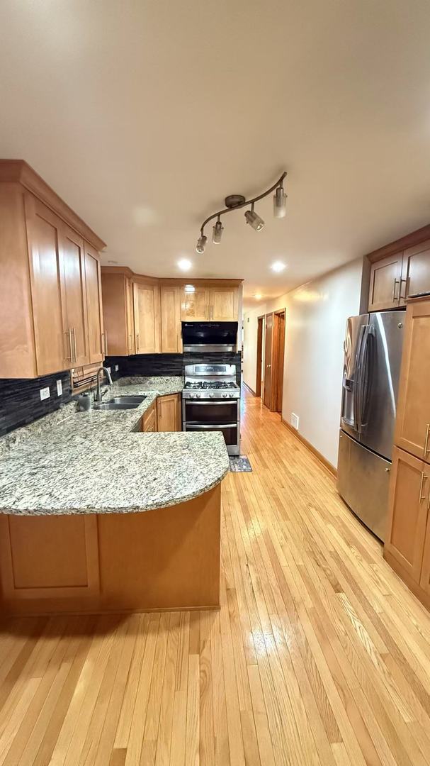 kitchen featuring light wood-style flooring, a peninsula, a sink, appliances with stainless steel finishes, and light stone countertops