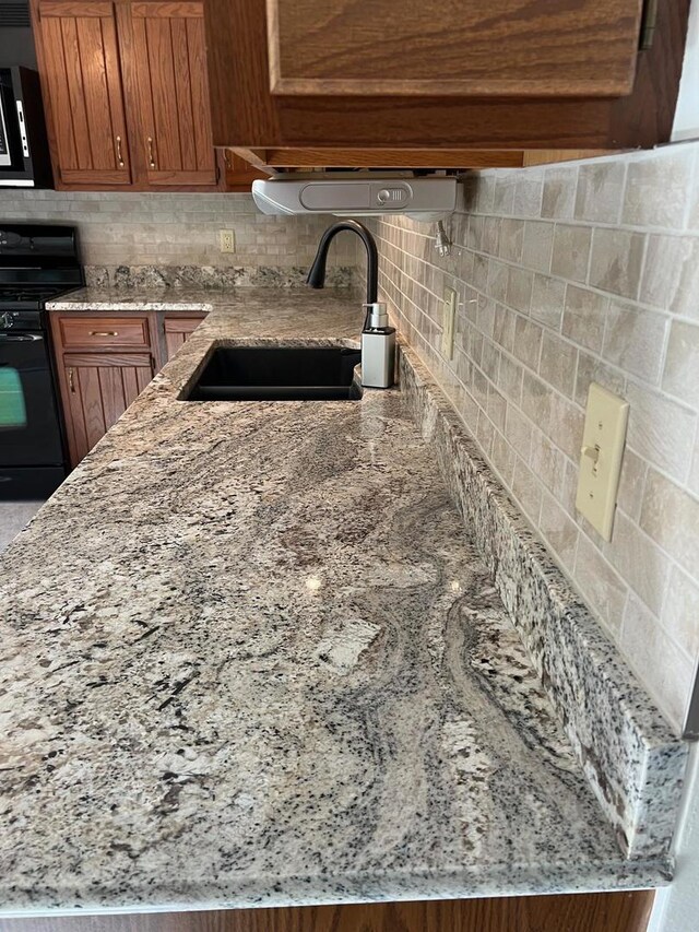 kitchen with light stone countertops, sink, black range, and backsplash