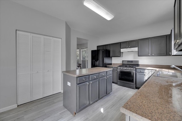 kitchen with black fridge with ice dispenser, light hardwood / wood-style flooring, sink, stainless steel range with gas stovetop, and a center island