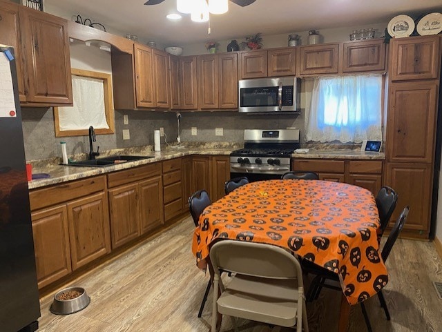 kitchen with light hardwood / wood-style flooring, stainless steel appliances, light stone countertops, and sink