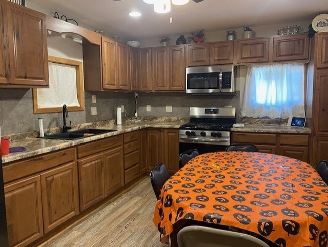 kitchen featuring ceiling fan, appliances with stainless steel finishes, light wood-type flooring, sink, and light stone counters