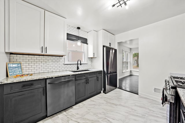 kitchen with appliances with stainless steel finishes, sink, white cabinetry, decorative light fixtures, and light stone counters