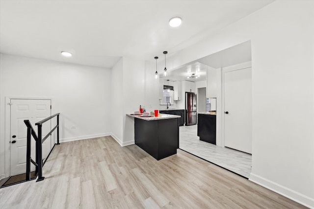 kitchen featuring kitchen peninsula, decorative light fixtures, light wood-type flooring, white cabinetry, and stainless steel refrigerator