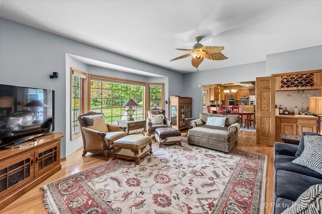 living room with bar, light wood-type flooring, and ceiling fan