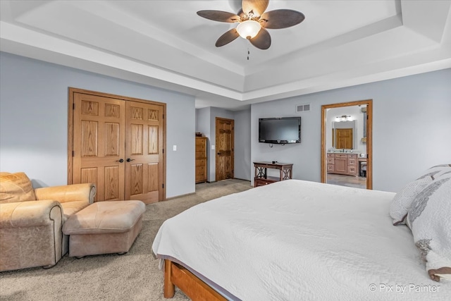 bedroom featuring ceiling fan, a tray ceiling, connected bathroom, a closet, and light colored carpet