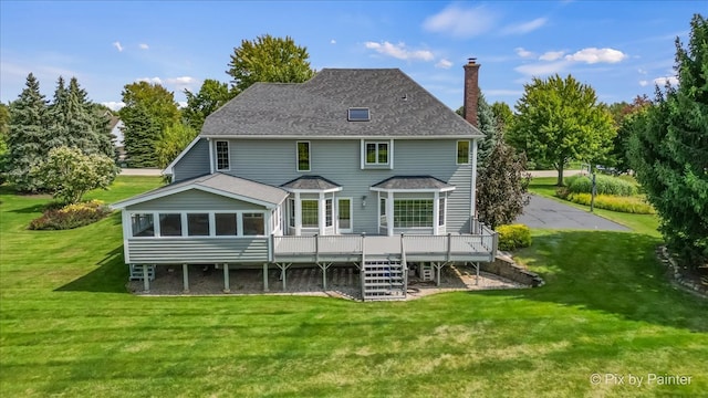 rear view of property featuring a deck, a sunroom, and a lawn