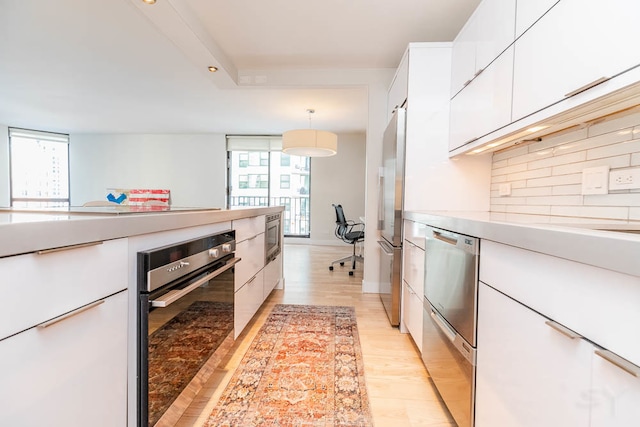 kitchen featuring white cabinets, tasteful backsplash, appliances with stainless steel finishes, light wood-type flooring, and pendant lighting