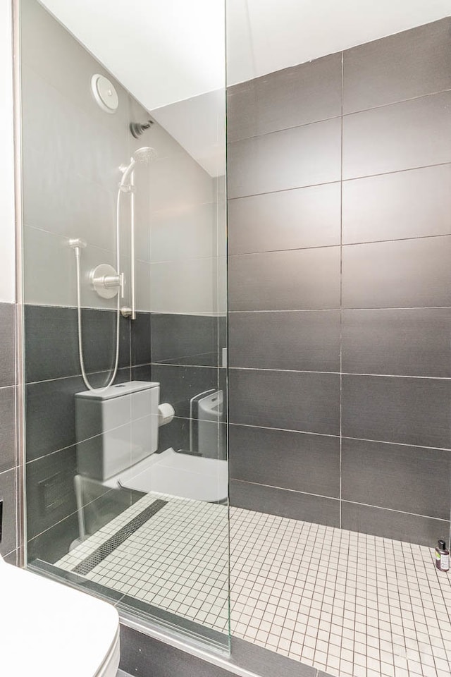 bathroom featuring toilet, tile walls, and tiled shower