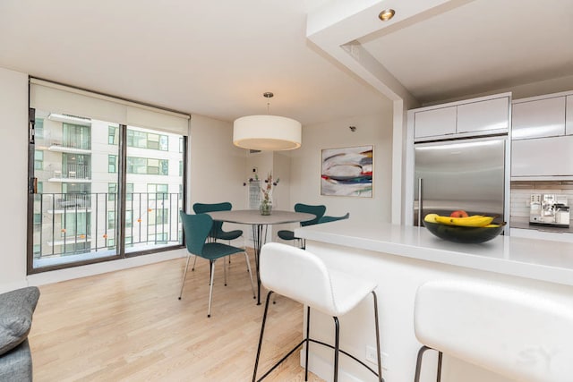 kitchen featuring a breakfast bar, white cabinetry, light wood-type flooring, built in fridge, and pendant lighting