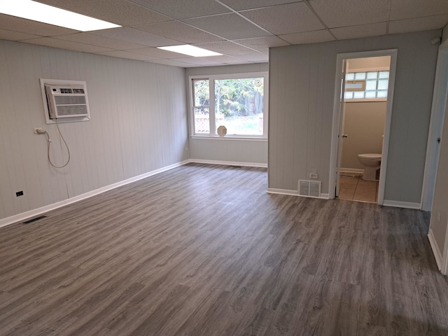 interior space with an AC wall unit, dark hardwood / wood-style flooring, and a drop ceiling