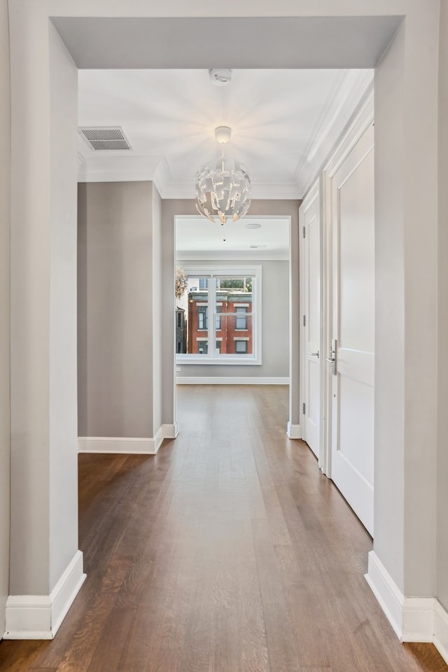 corridor with ornamental molding, hardwood / wood-style flooring, and an inviting chandelier