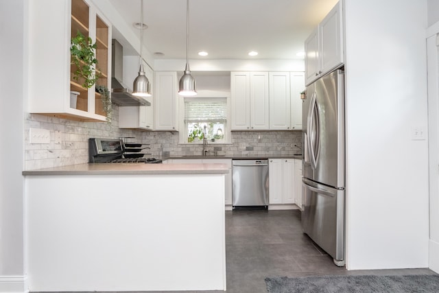 kitchen featuring wall chimney exhaust hood, hanging light fixtures, kitchen peninsula, white cabinetry, and appliances with stainless steel finishes