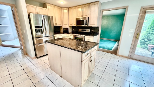 kitchen featuring appliances with stainless steel finishes, light tile patterned flooring, a center island, dark stone counters, and decorative backsplash