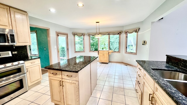 kitchen with light brown cabinets, dark stone countertops, light tile patterned flooring, decorative light fixtures, and appliances with stainless steel finishes