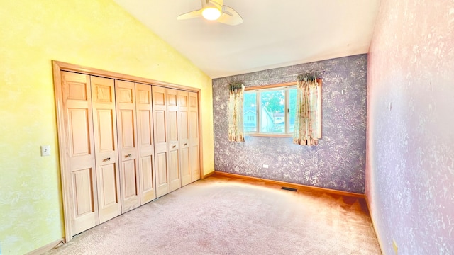 unfurnished bedroom with vaulted ceiling, light colored carpet, a closet, and ceiling fan