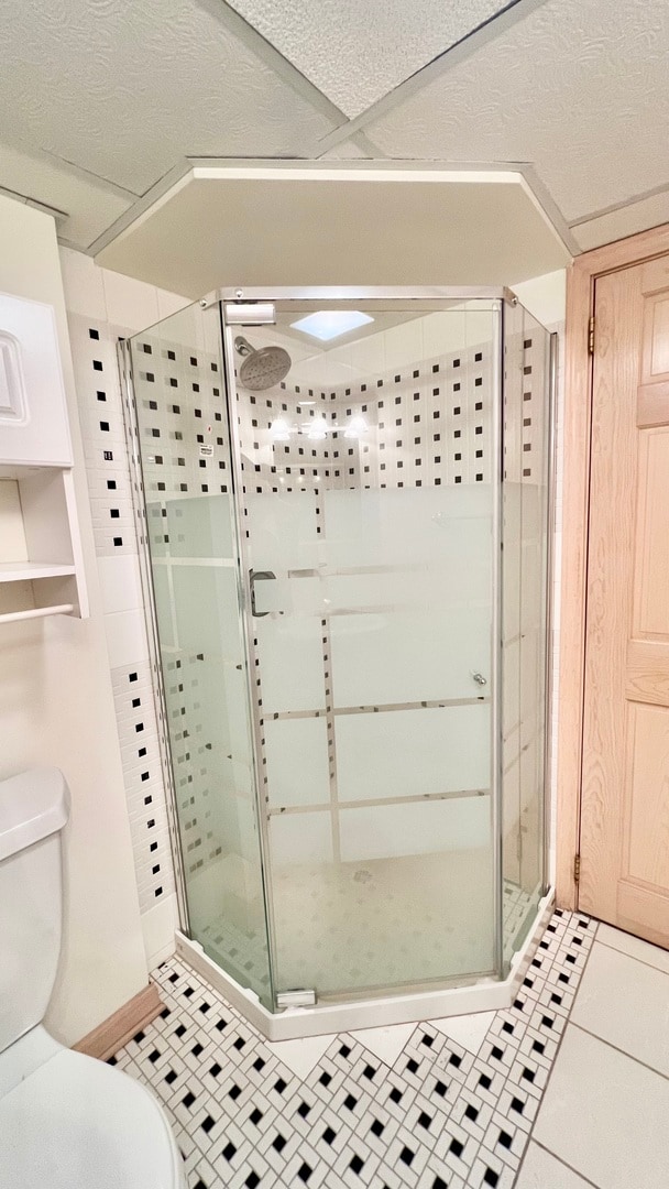 bathroom featuring tile patterned floors, a shower with shower door, and toilet