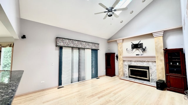 living room featuring ceiling fan, a premium fireplace, high vaulted ceiling, a skylight, and light hardwood / wood-style floors