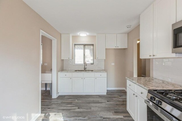 kitchen featuring white cabinets, tasteful backsplash, a sink, and wood finished floors