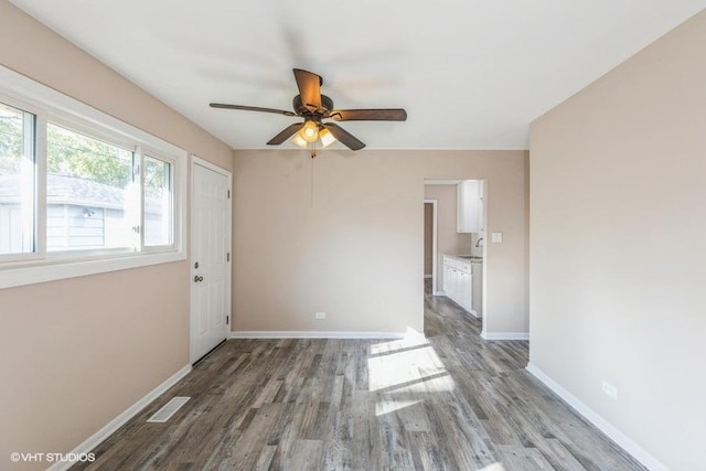 empty room with baseboards, ceiling fan, visible vents, and wood finished floors