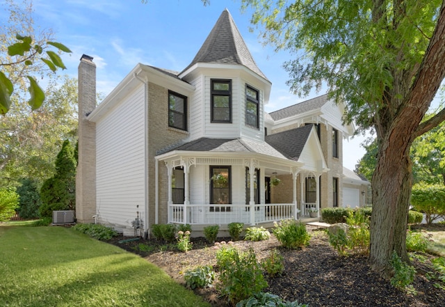 victorian house featuring covered porch, a front yard, central air condition unit, and a garage