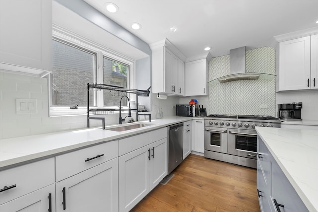 kitchen with white cabinets, light hardwood / wood-style flooring, sink, wall chimney exhaust hood, and stainless steel appliances